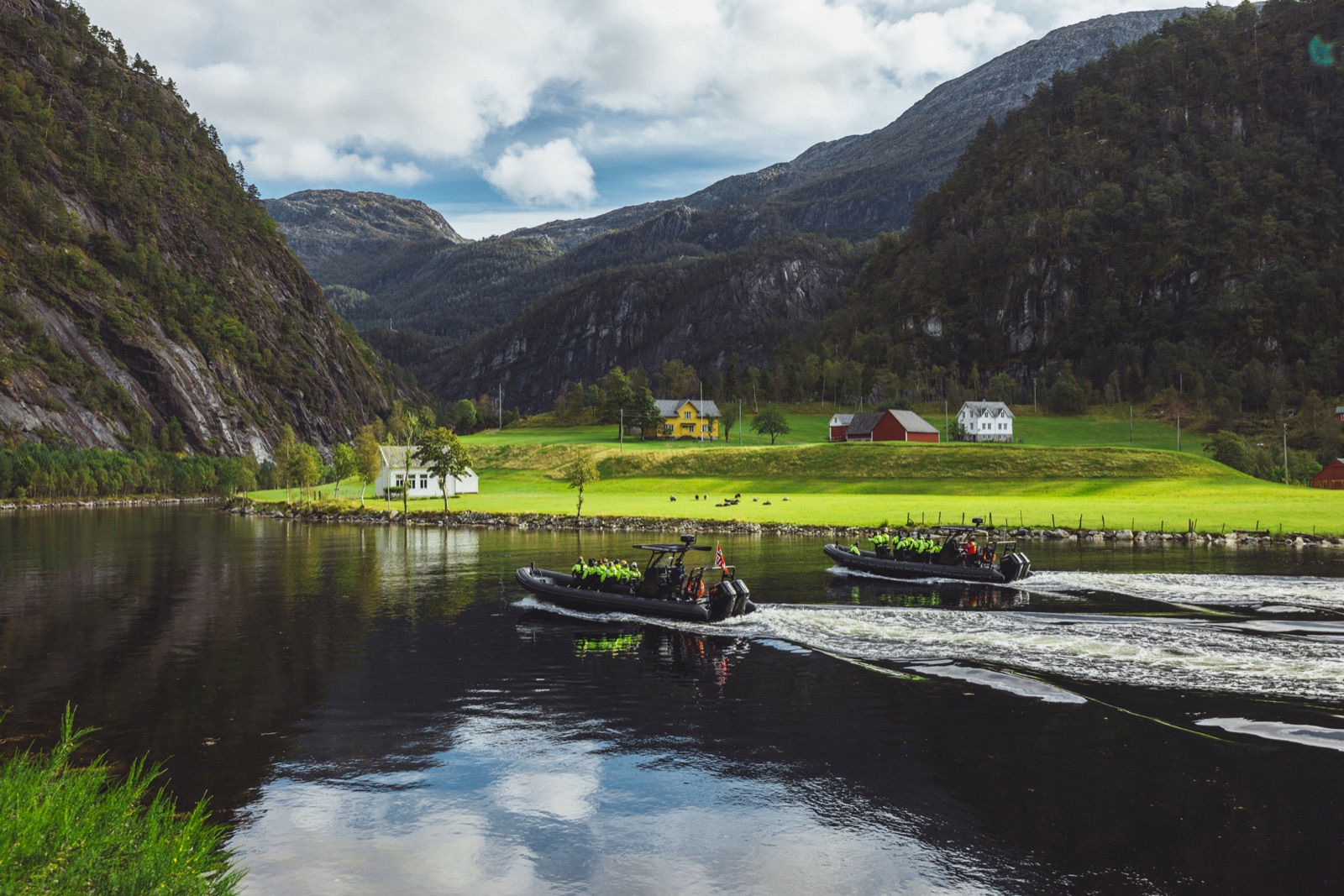 Two Bergen Fjord Safari RIBs cruising past a fjord-side farm